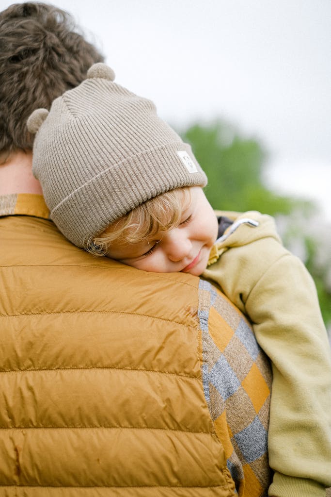 Father carries sleeping child on shoulder outdoors, conveying warmth and care.